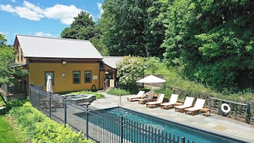 A yellow building with a swimming pool, surrounded by greenery and a fenced patio area with lounge chairs.