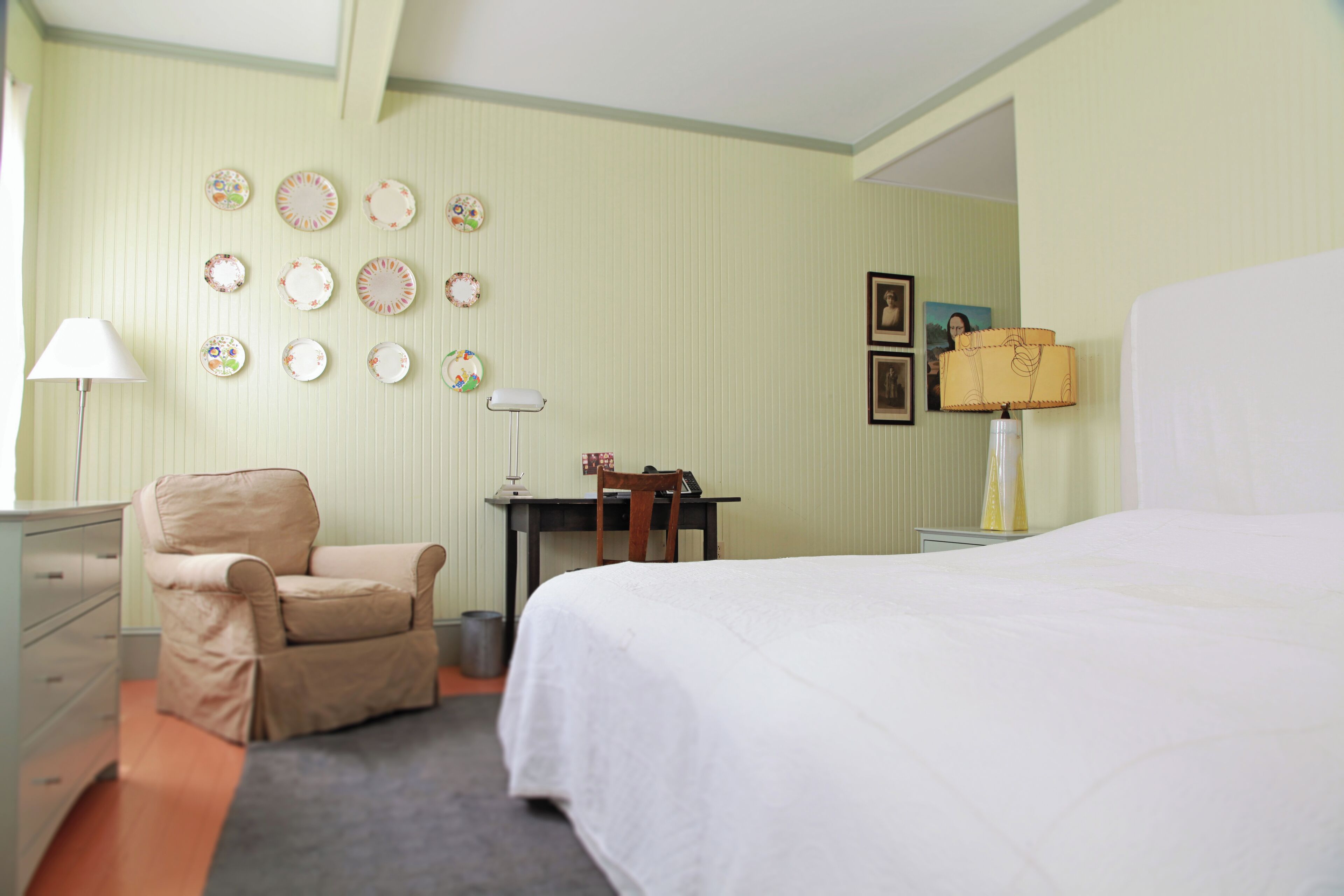 Habitación de hotel con una cama, un escritorio, una silla y una pared con adornos de platos.