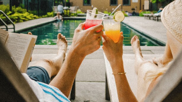 Two people relaxing by a poolside with drinks, a building in the background, and a clear sky. - The Porches Inn at Mass MoCA (North Adams)