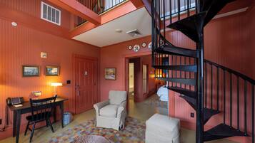 Una habitación con un escritorio, una silla, un reposapiés y una escalera en espiral negra.