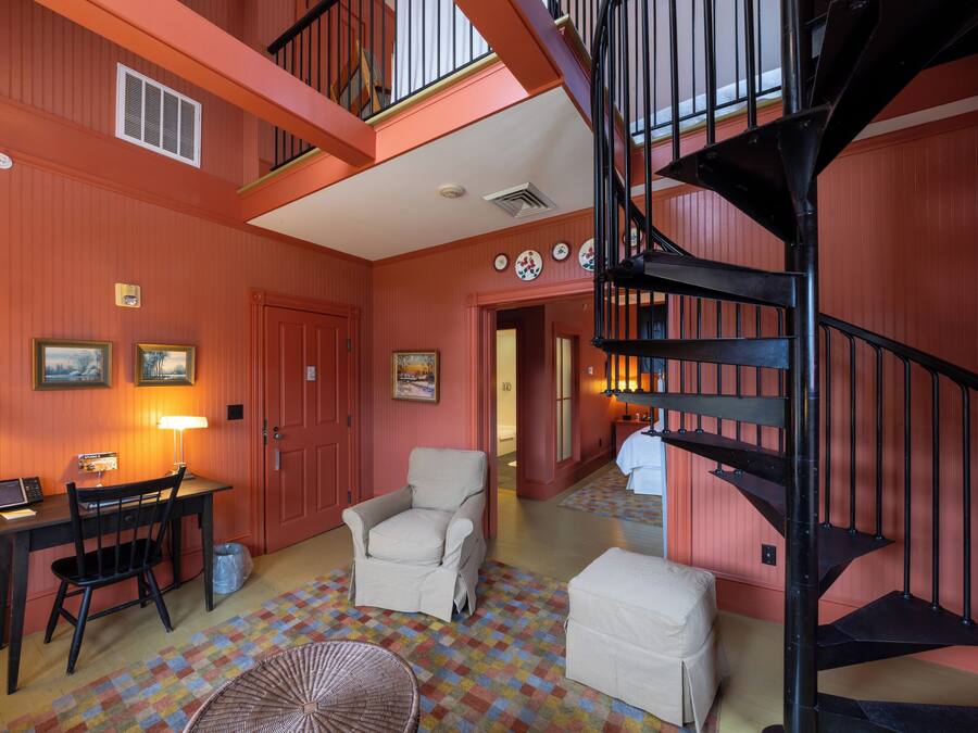 Una habitación con un escritorio, una silla, un reposapiés y una escalera en espiral negra.