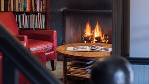 A cozy living room with a fireplace, a red armchair, a bookshelf, and a coffee table. - The Porches Inn at Mass MoCA (North Adams)
