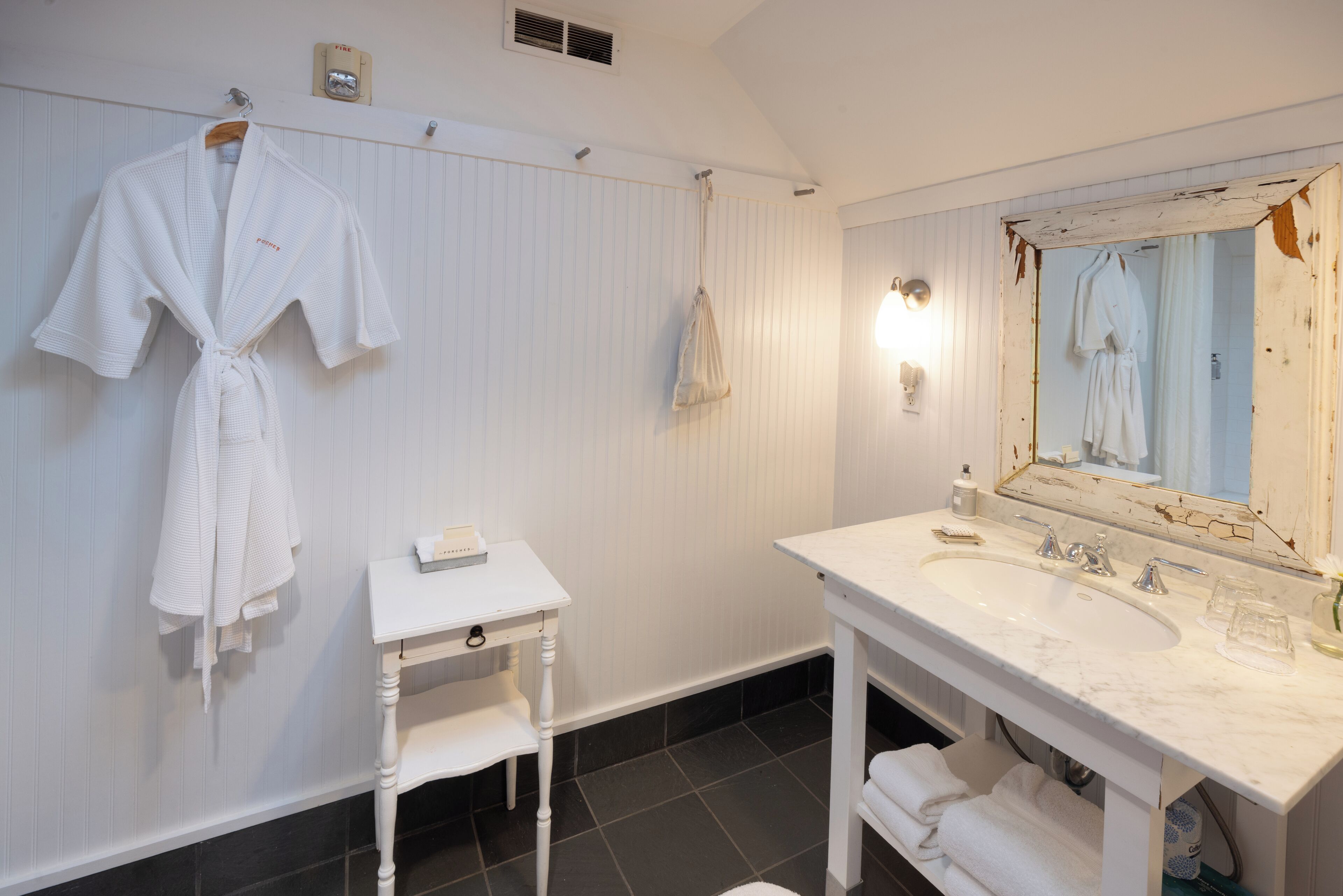 A bathroom with a white sink, mirror, and two white robes hanging on the wall.