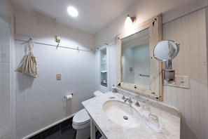 Bathroom features a toilet, sink, and mirror, with a towel rack and toiletries on a shelf.
