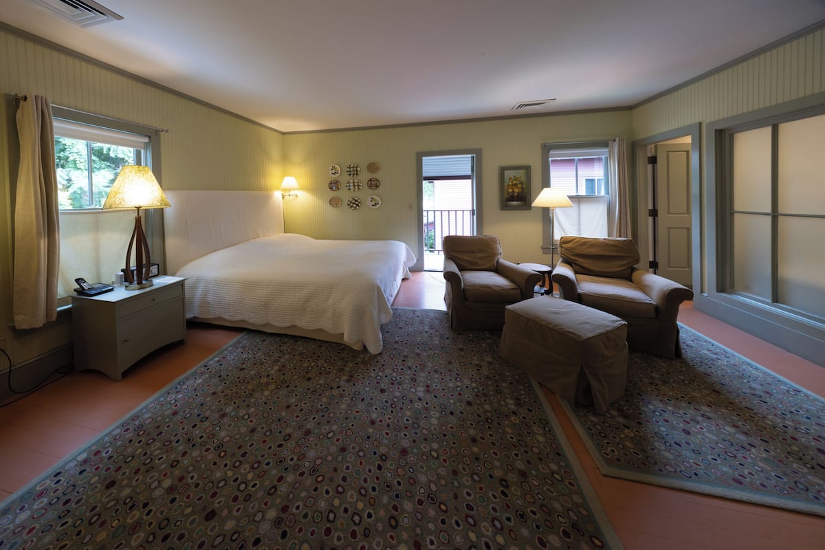 Une chambre d’hôtel avec un grand lit, deux chaises, une petite table et une fenêtre avec des rideaux.