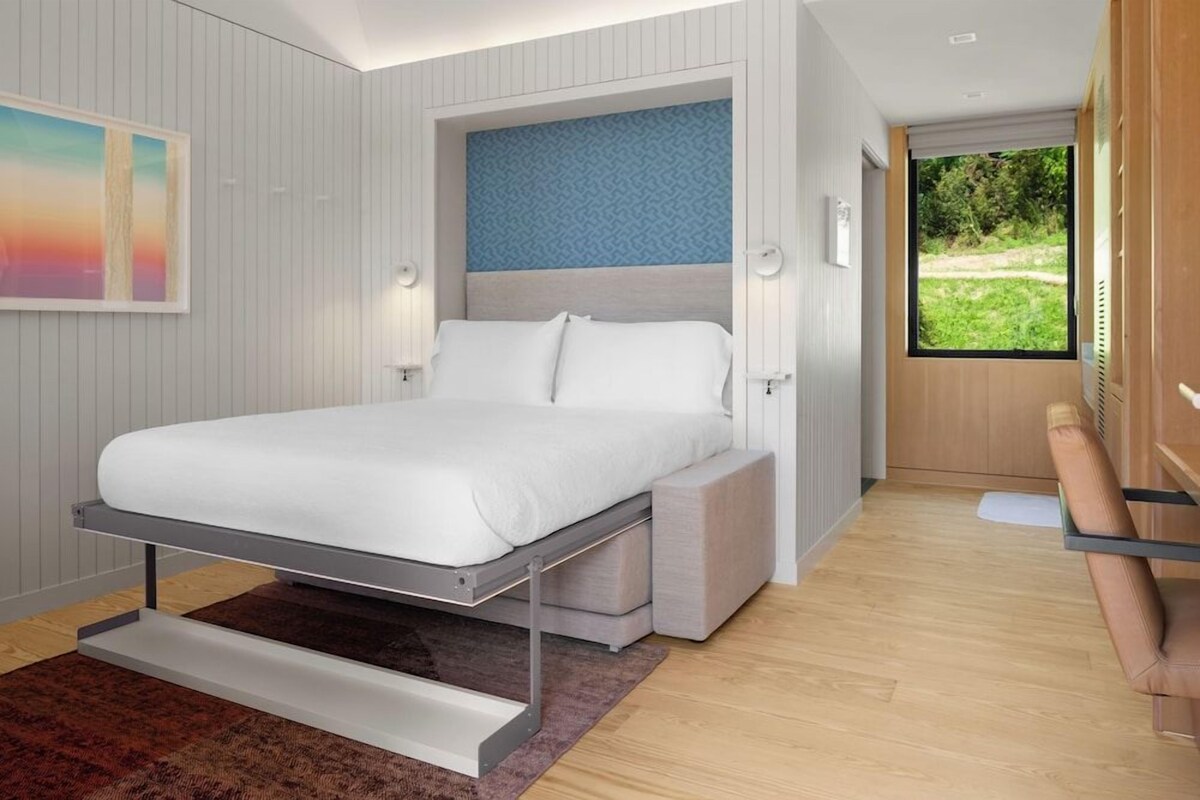 A modern bedroom with a bed, bedside tables, a window, and a view of greenery.
