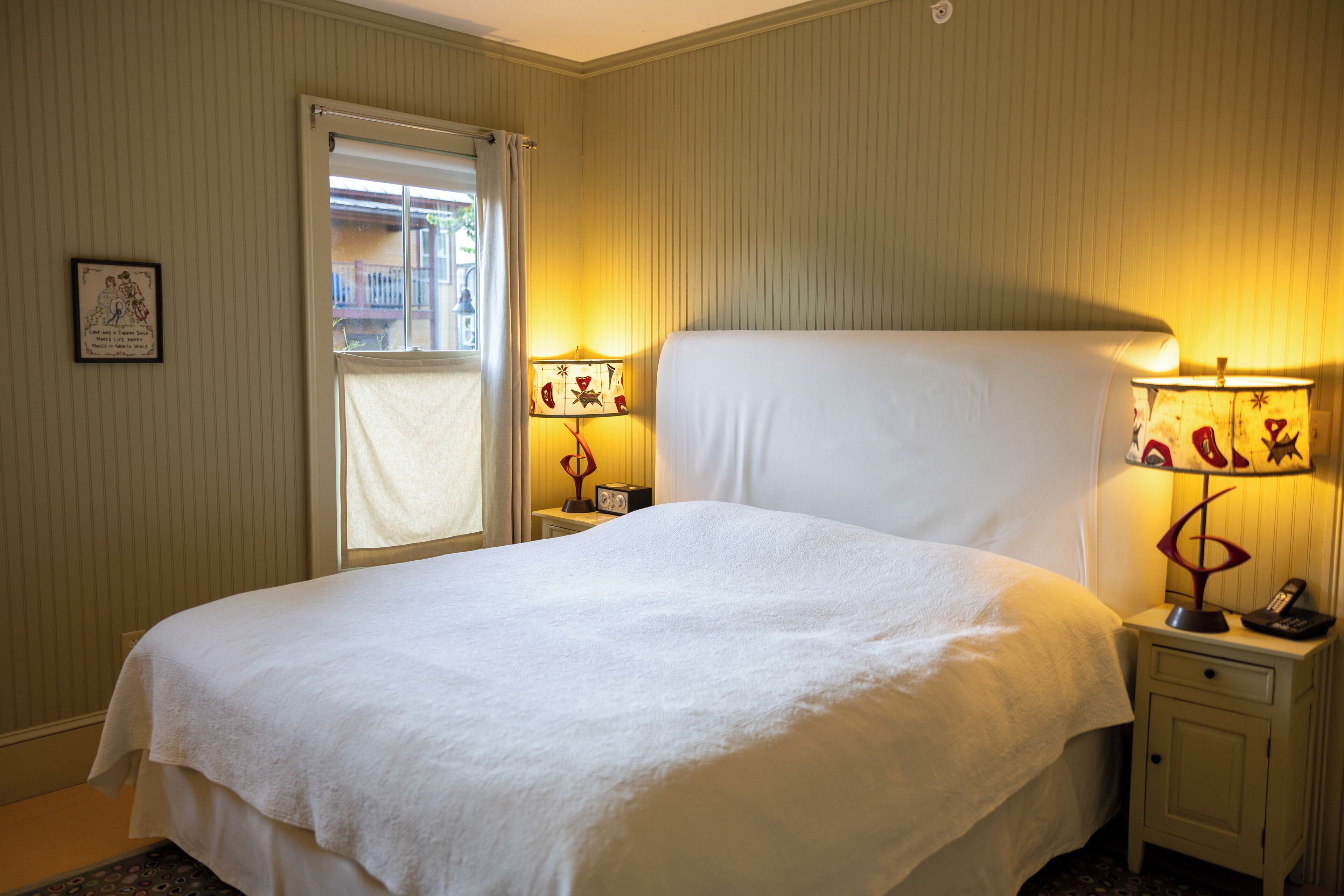 Una cama bien hecha en una habitación de hotel, con dos mesitas de noche, cada una con una lámpara y un teléfono.