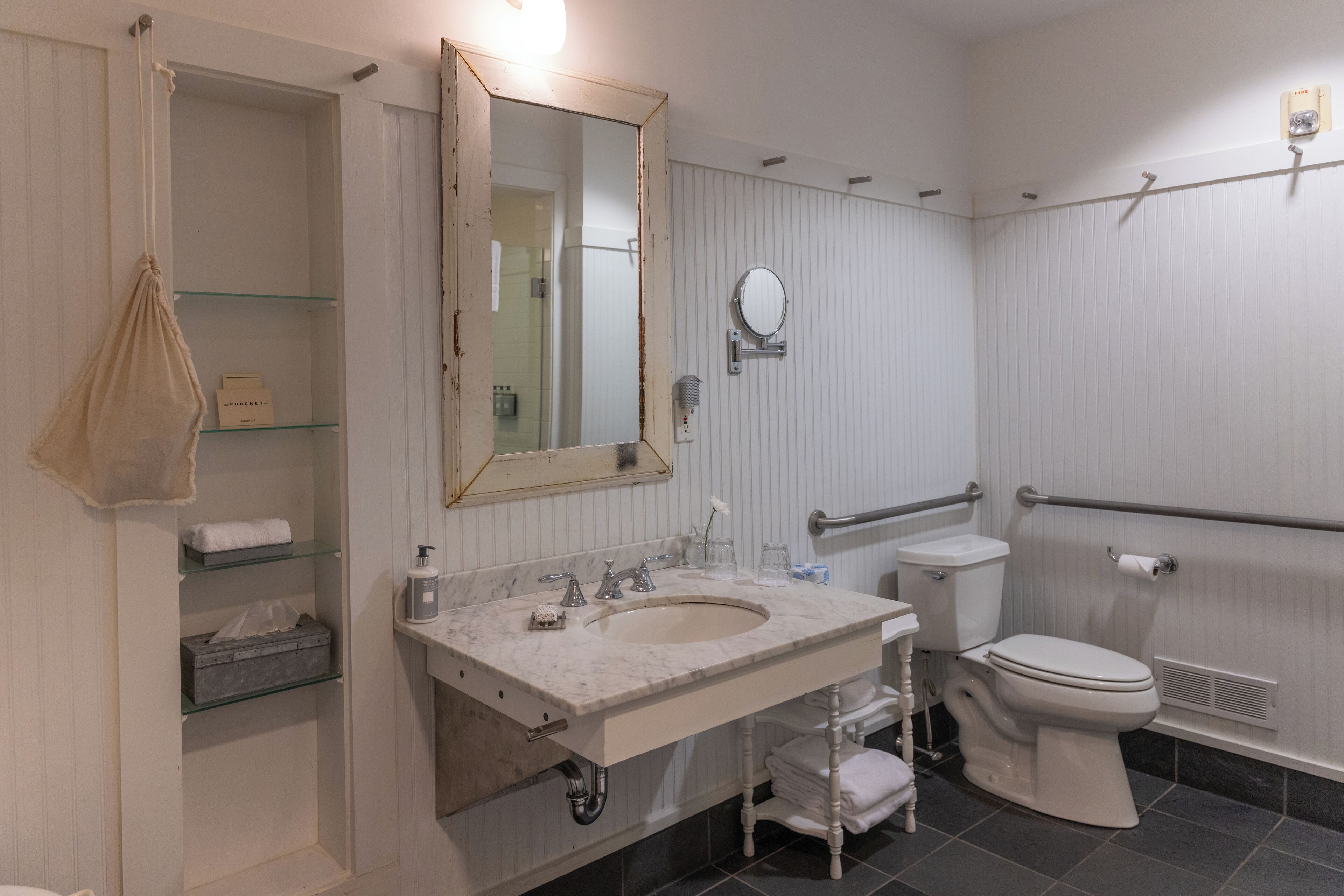 Une salle de bain avec un lavabo en marbre, un grand miroir, des toilettes et une étagère en verre.