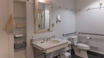 Une salle de bain avec un lavabo en marbre, un grand miroir, des toilettes et une étagère en verre.