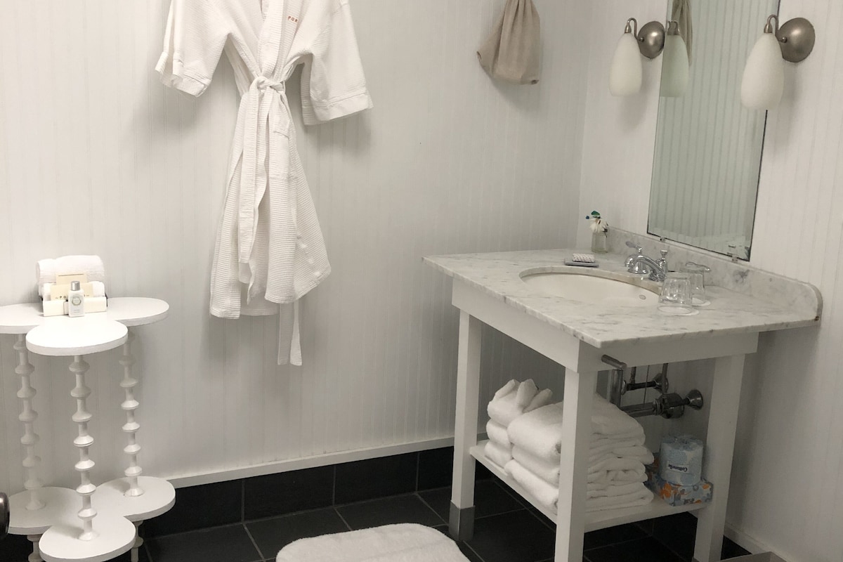 Un baño con lavamanos blanco, espejo, toallero y una alfombra de baño blanca.