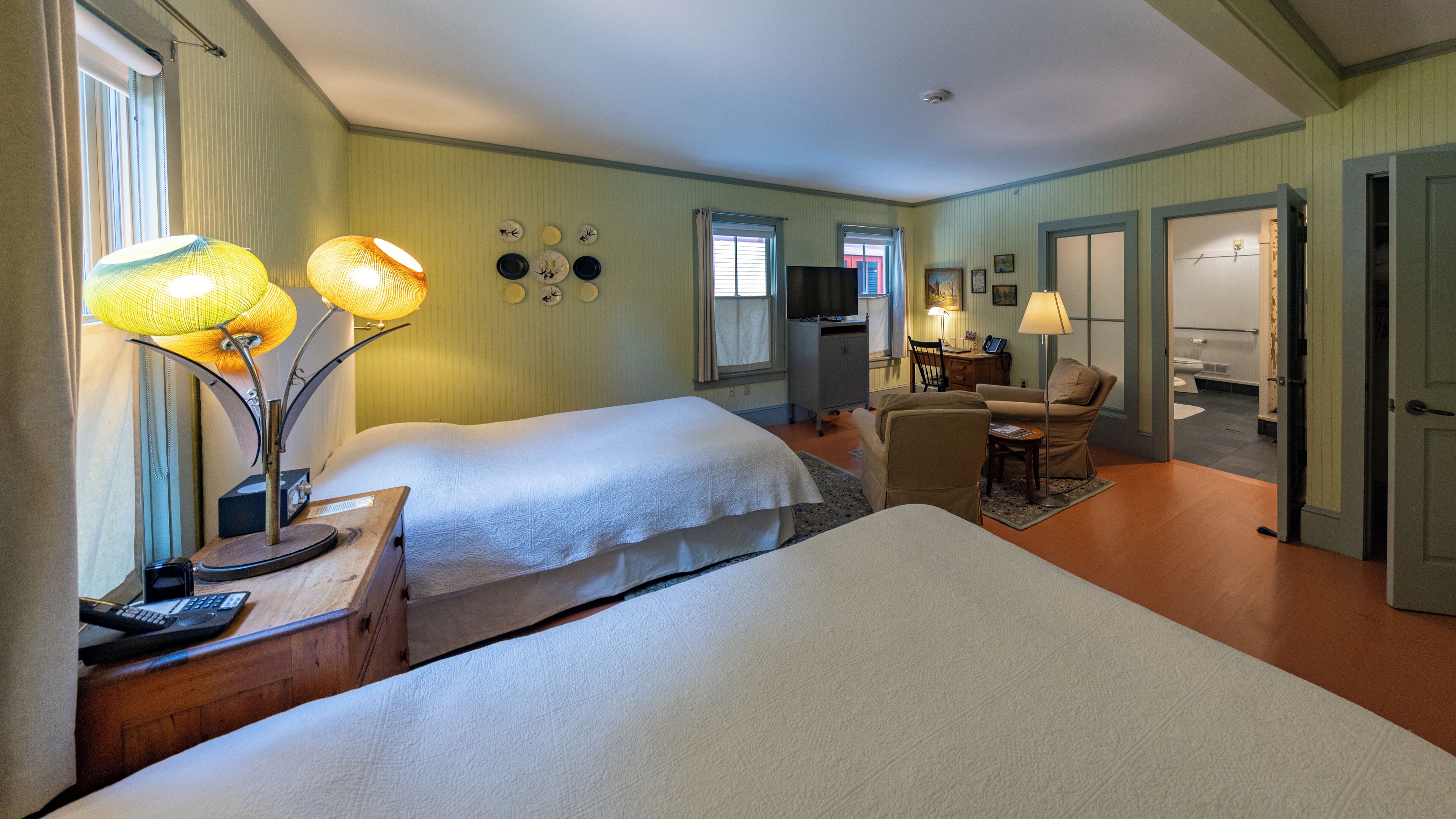 Habitación de hotel con dos camas, un escritorio con computadora, una silla y televisión.