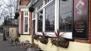 An outdoor seating area with tables and chairs, a sign advertising fresh coffee, and a brick building facade. - The Stag Enfield (Enfield)