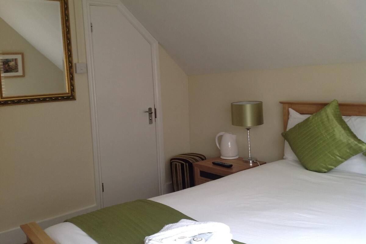 Une chambre d’hôtel avec un lit, une table de chevet, une lampe, un oreiller vert, une serviette blanche et un miroir.
