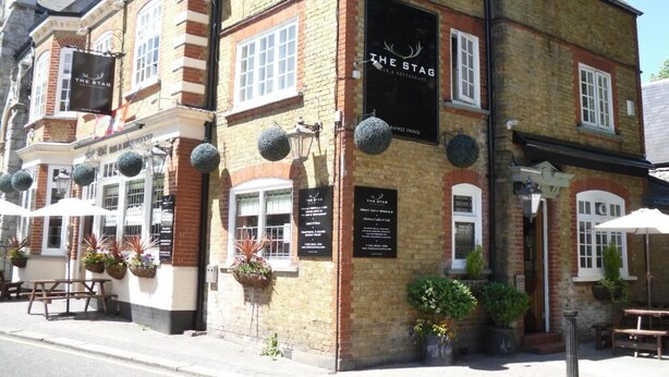 A traditional brick building with a sign reading "The Stag Inn." It features outdoor seating with umbrellas and potted plants. - The Stag Enfield (Enfield)