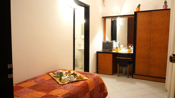 Habitación de hotel pequeña con cama, escritorio, computadora, espejo y armario.