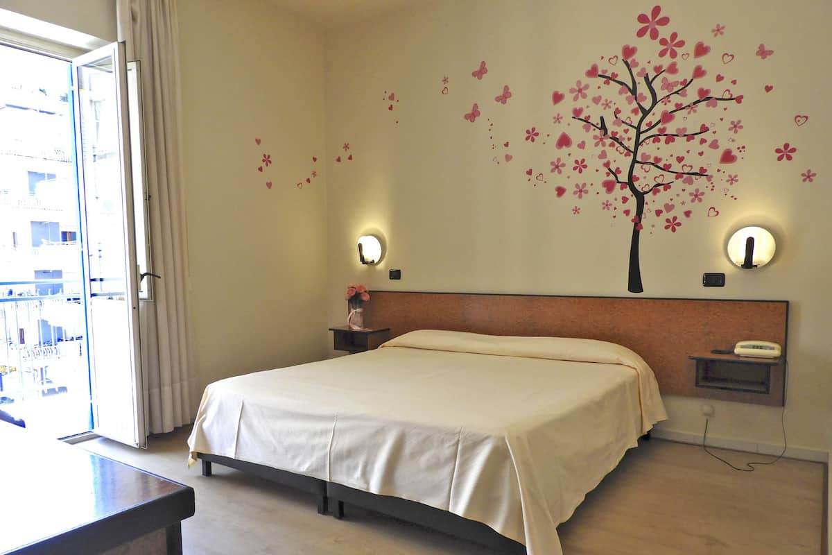 Ein Hotelzimmer mit einem Bett, Nachttischen, einem an der Wand befestigten Telefon und einem Fenster mit Vorhängen.
