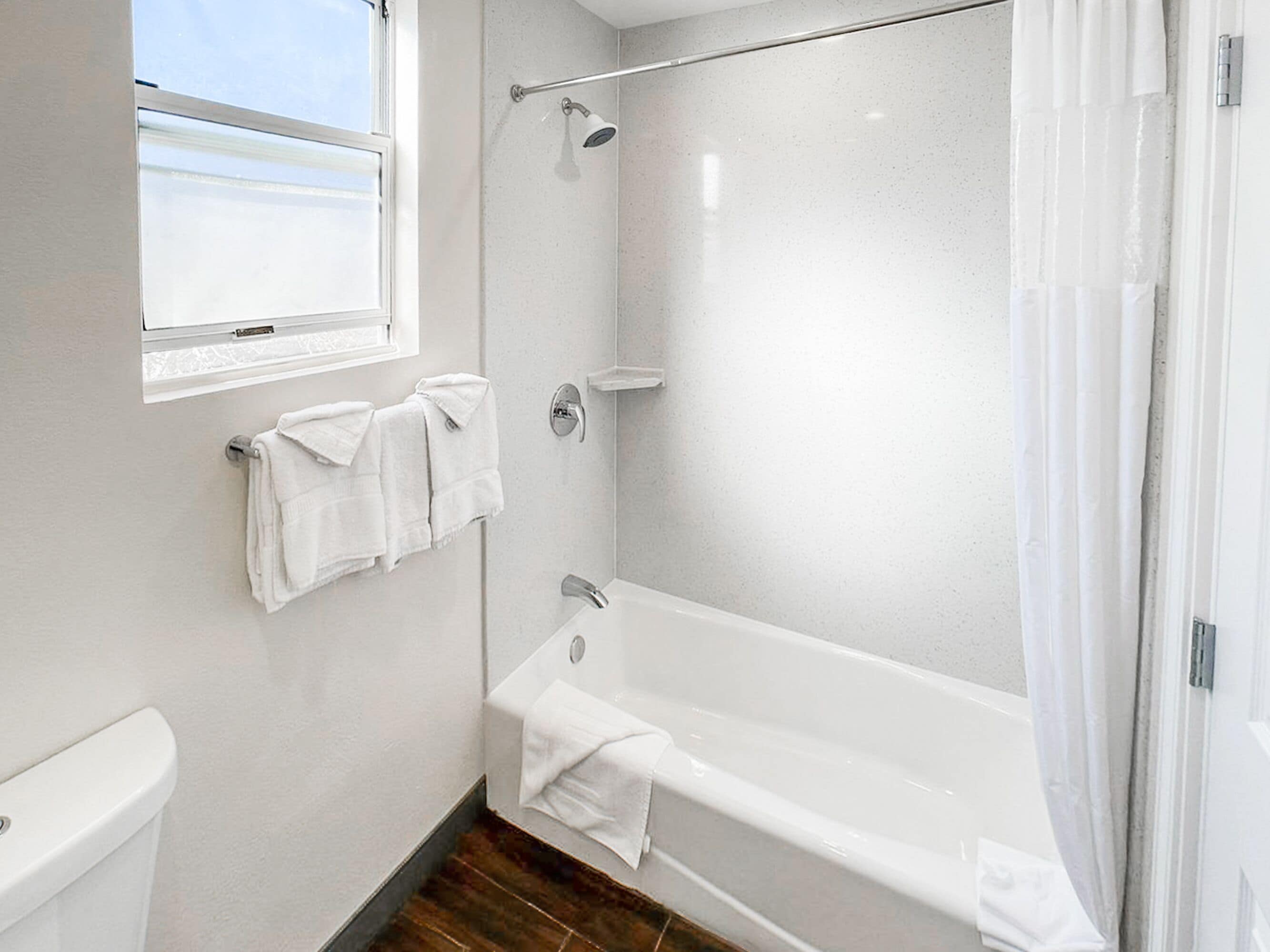Un baño moderno con bañera, ducha y retrete. Hay dos toallas colgadas en la pared.