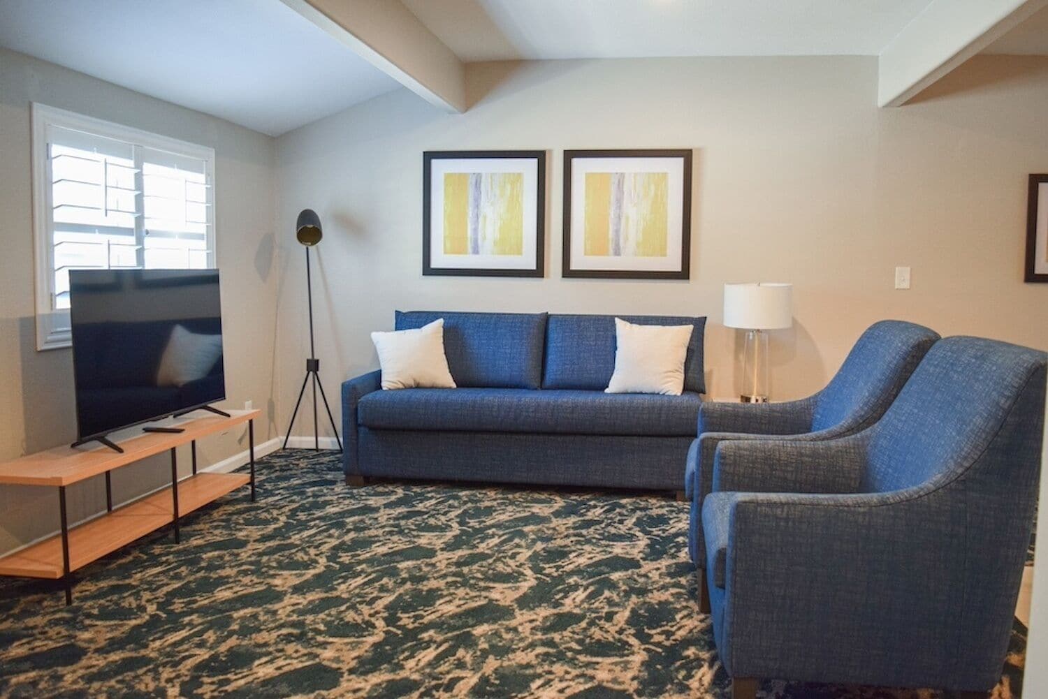 A living room with a sofa, a TV on a stand, a floor lamp, and two framed pictures on the wall.