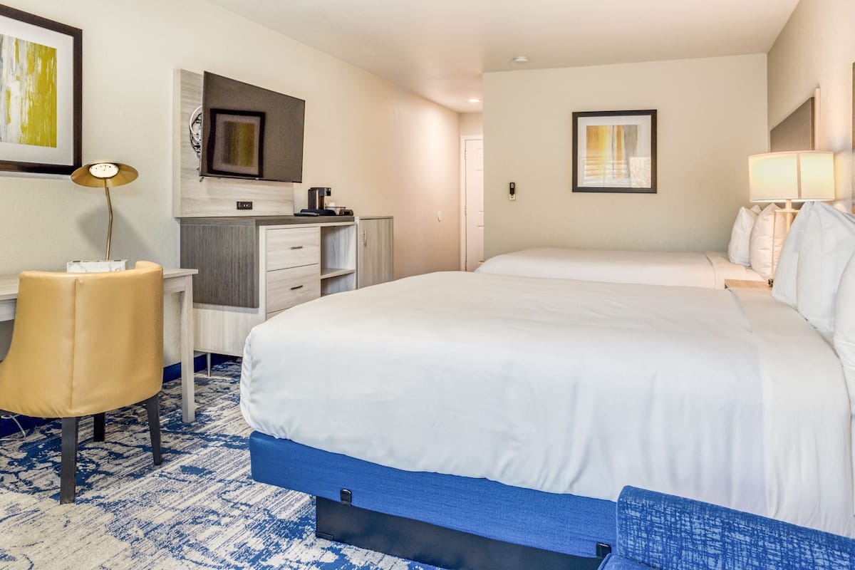 A hotel room with a large bed, a desk with a chair, a small kitchenette, and a bathroom door.