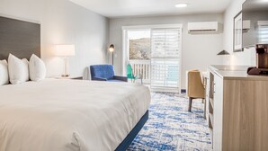 Ein Hotelzimmer mit einem großen Bett, einem Schreibtisch, einem Stuhl, einer Lampe und Blick durch die Tür.
