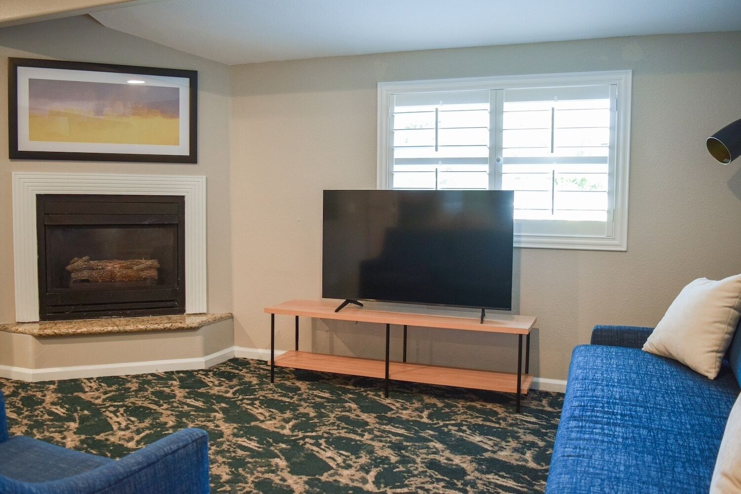 A living room with a fireplace, a TV on a stand, a blue couch, and a patterned carpet.