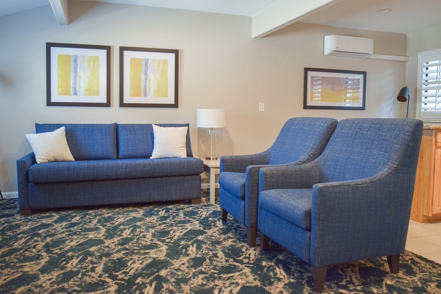 A living room with a sofa and two armchairs, a lamp, and two framed abstract paintings on the wall.