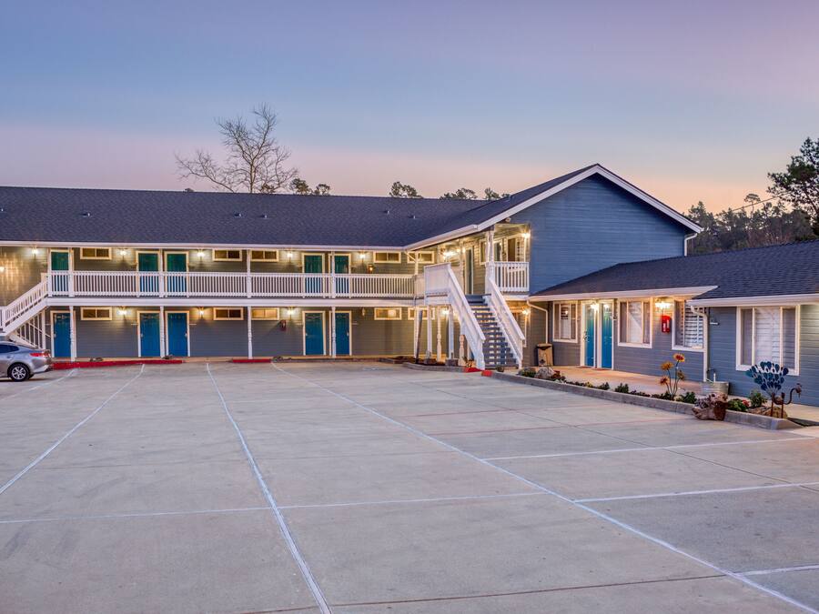 A motel with a central parking area, multiple rooms with balconies, and a staircase leading to the upper level.
