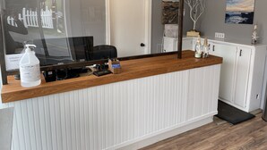 Ein Empfangsschalter mit Holzbeschlag, einer Wand mit weißen Verkleidungen, einer Tür, einem Computermonitor und einer kleinen Vitrine mit Dekoration.