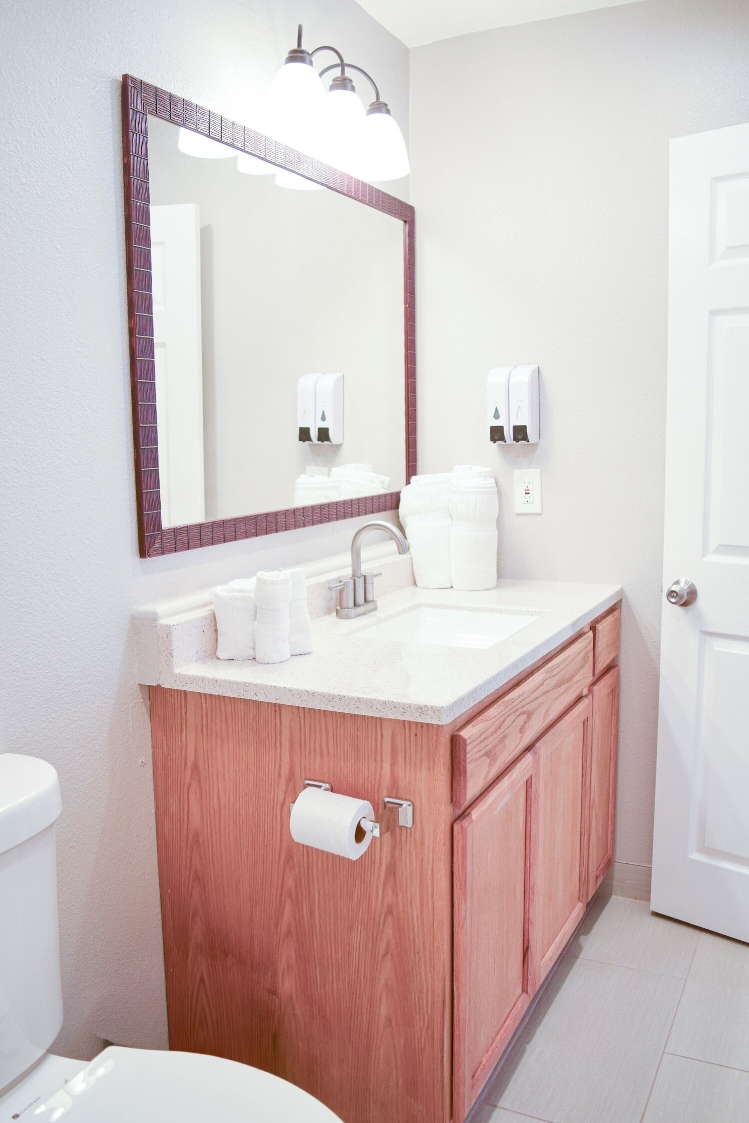 Une salle de bain avec un lavabo blanc, un miroir avec un cadre en bois, des toilettes et une porte.