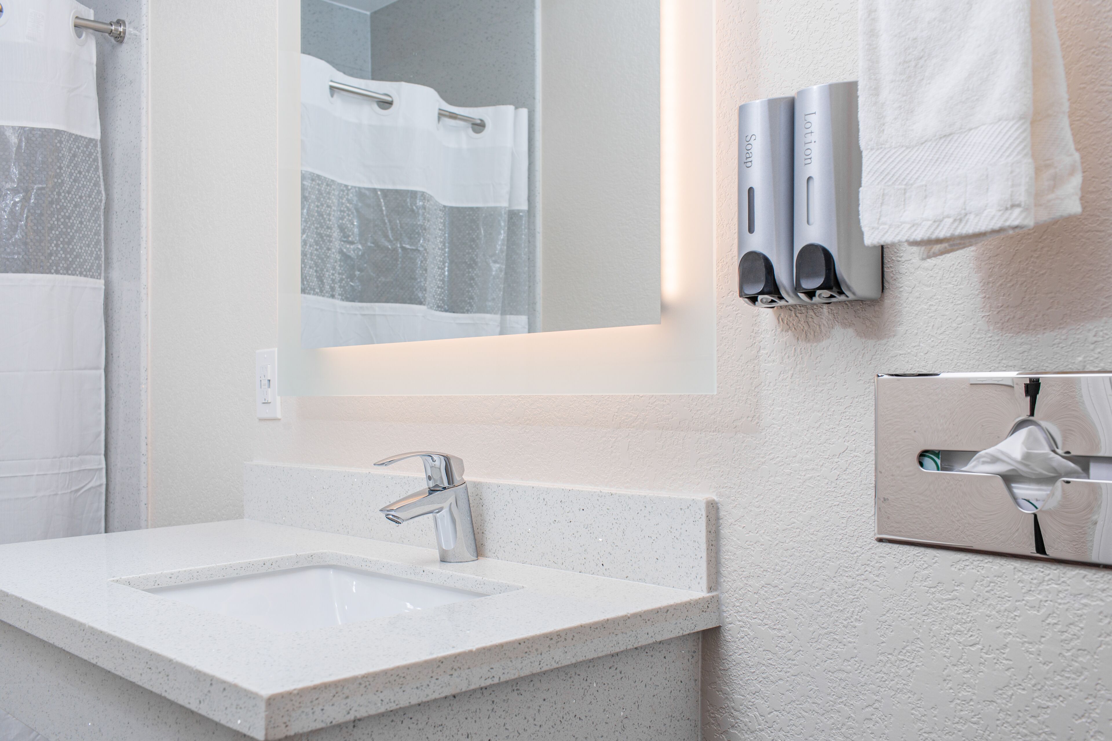 A bathroom with a white sink, a mirror, a towel dispenser, and a towel rack.
