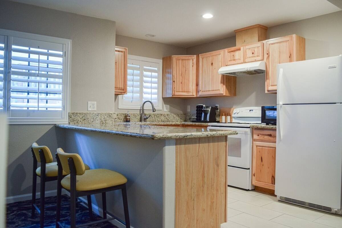 A kitchen with wooden cabinets, a granite countertop, a sink, a stove, and a refrigerator.