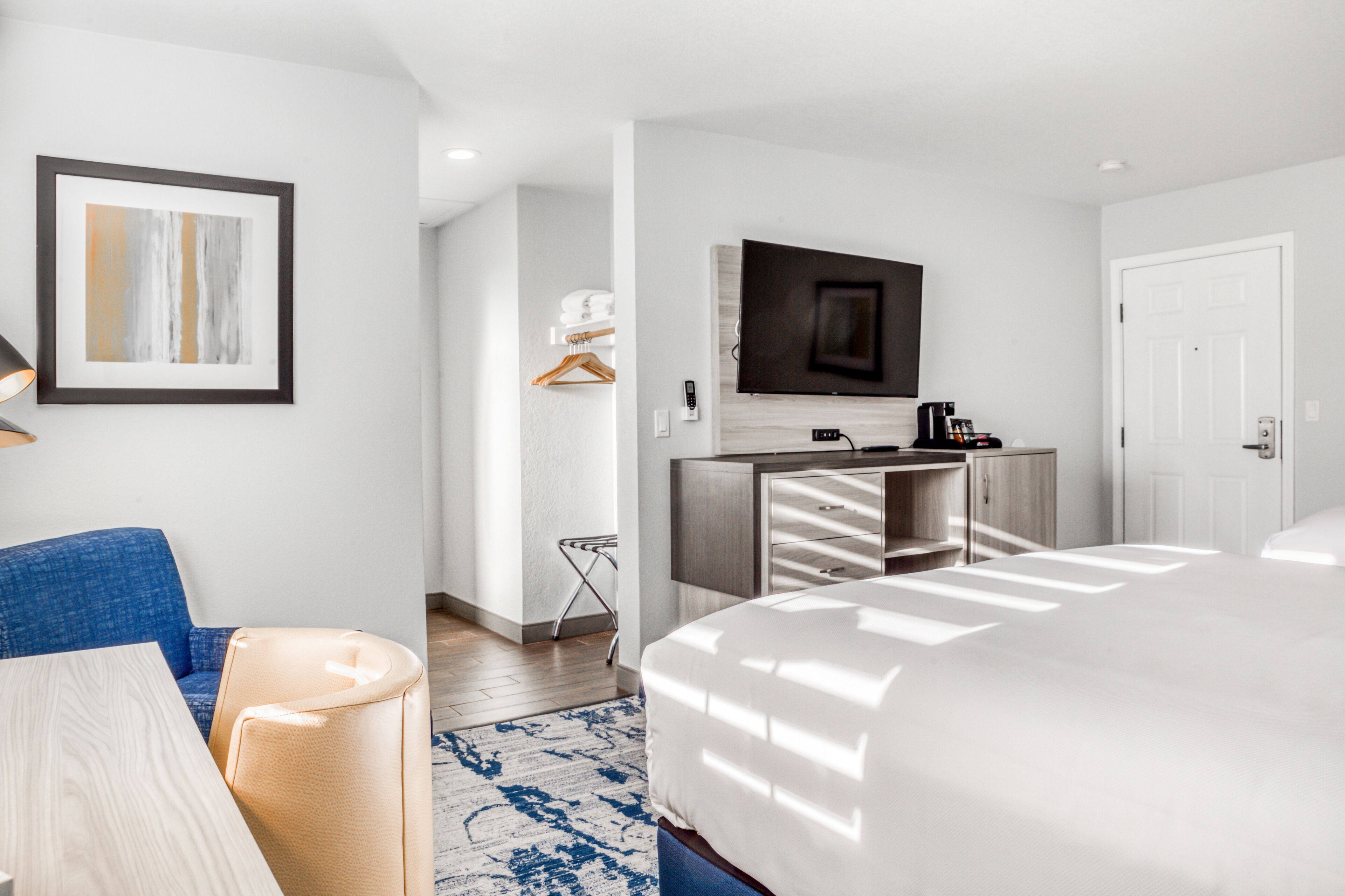 A modern hotel room with a large bed, a flat-screen TV mounted on the wall, a desk with a chair, and a blue sofa.