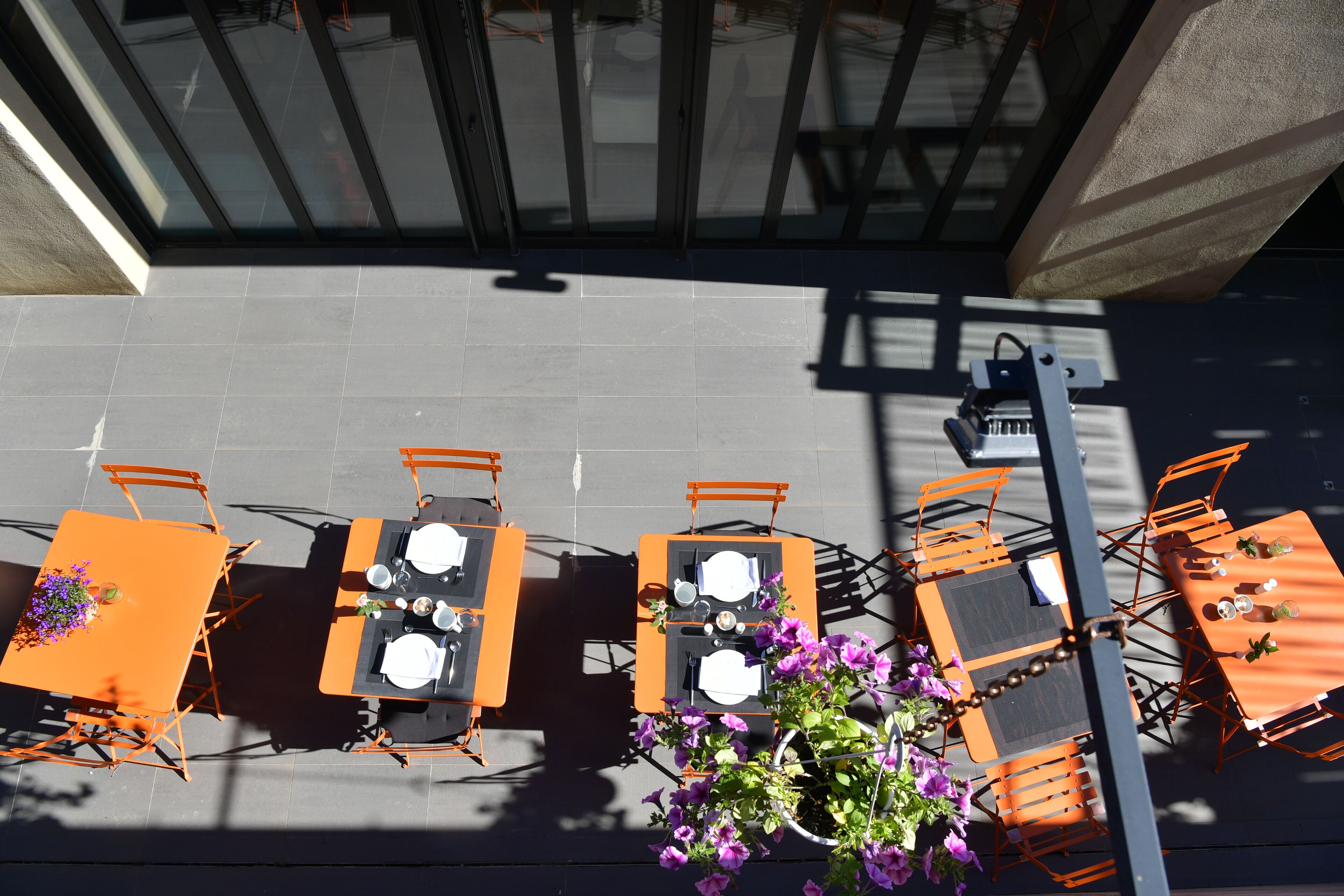 An outdoor seating area with tables and chairs arranged in a row, facing a building with large windows.