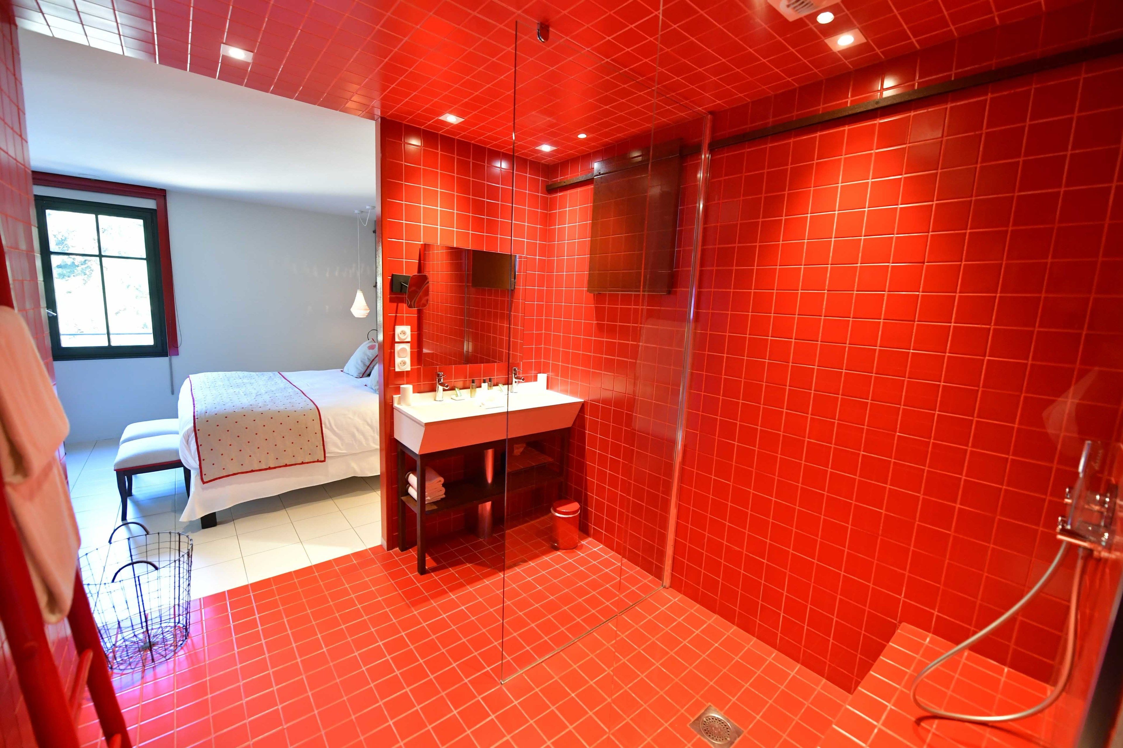 A bathroom with red tiles, a white sink, a mirror, and a shower area.