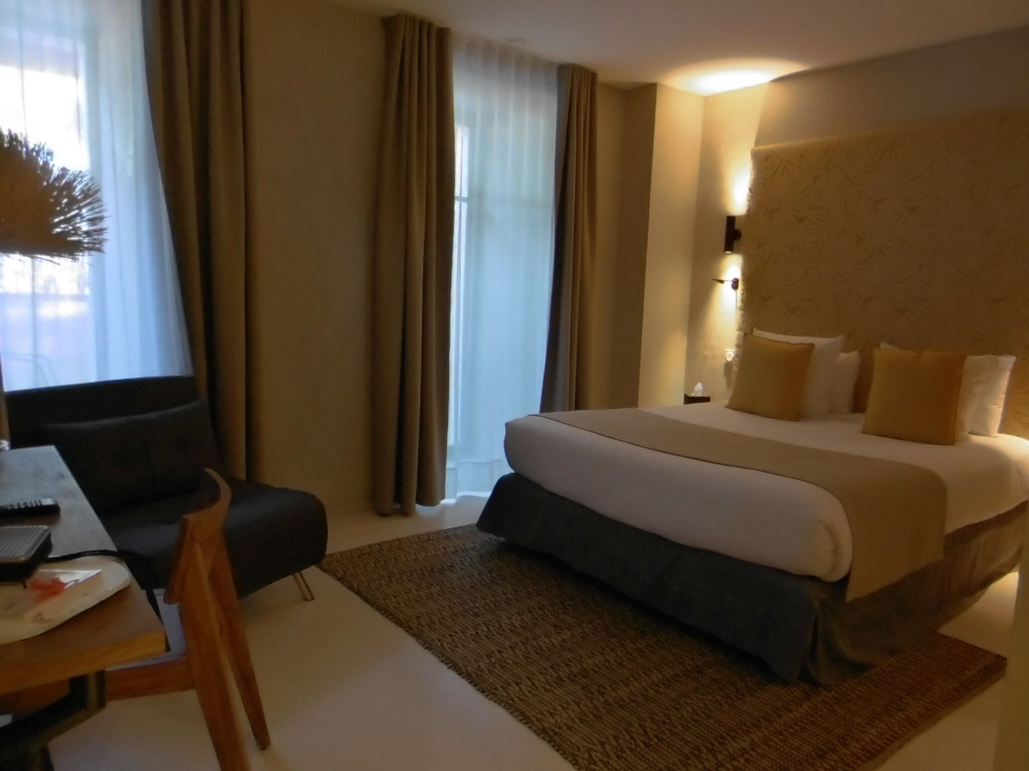 A hotel room with a bed, a desk with a laptop, a chair, and a window with curtains.
