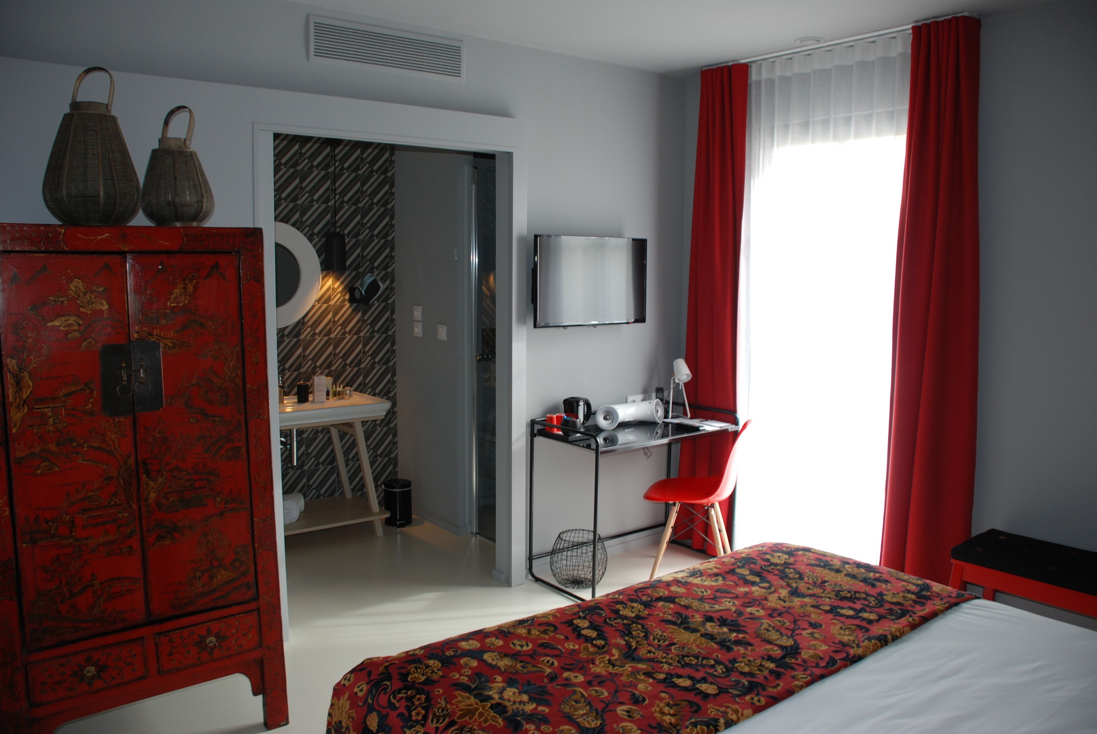 A hotel room with a bed, a desk with a chair, a television, and a wardrobe.
