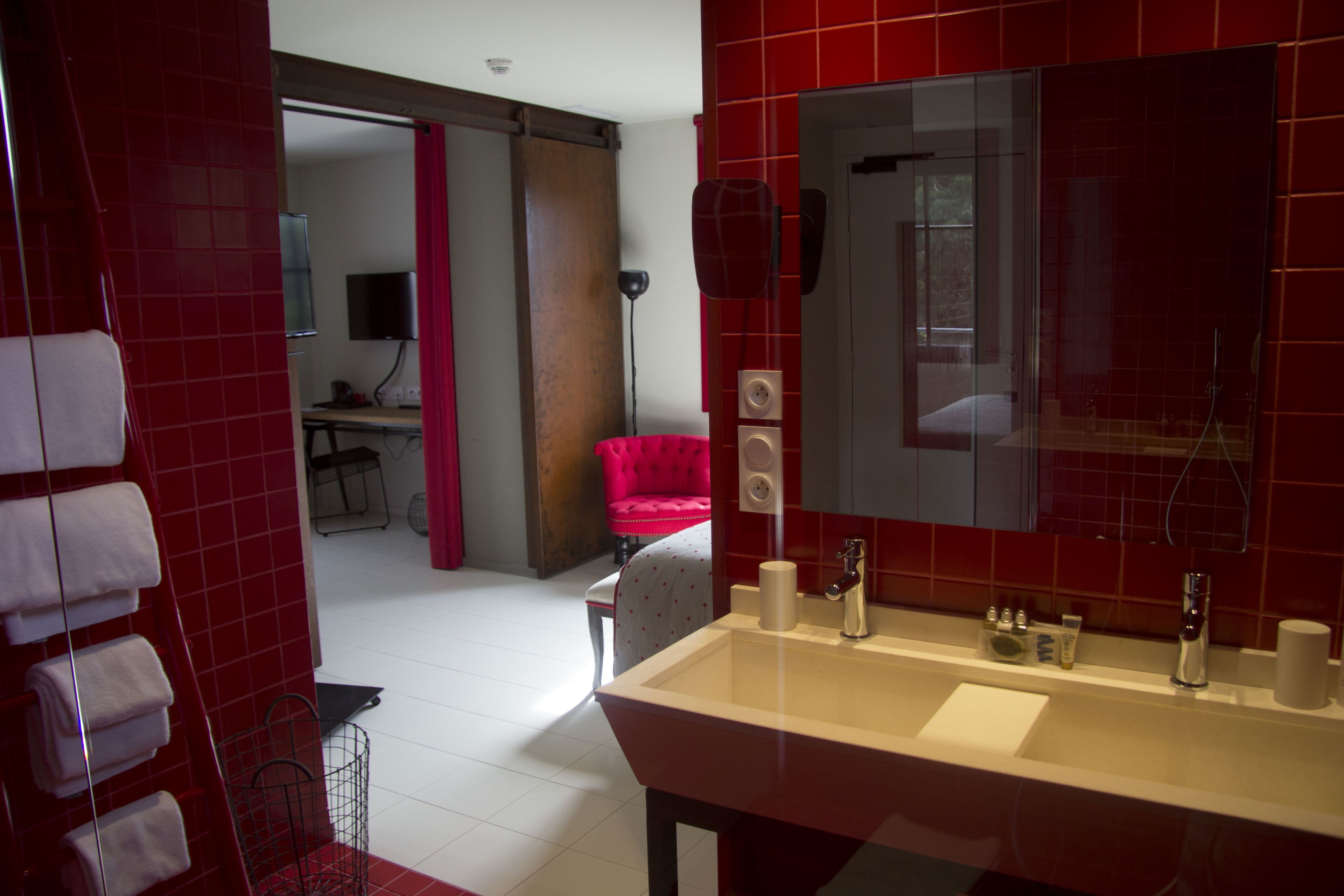 A modern bathroom with a large mirror, a sink, and a red-tiled wall.
