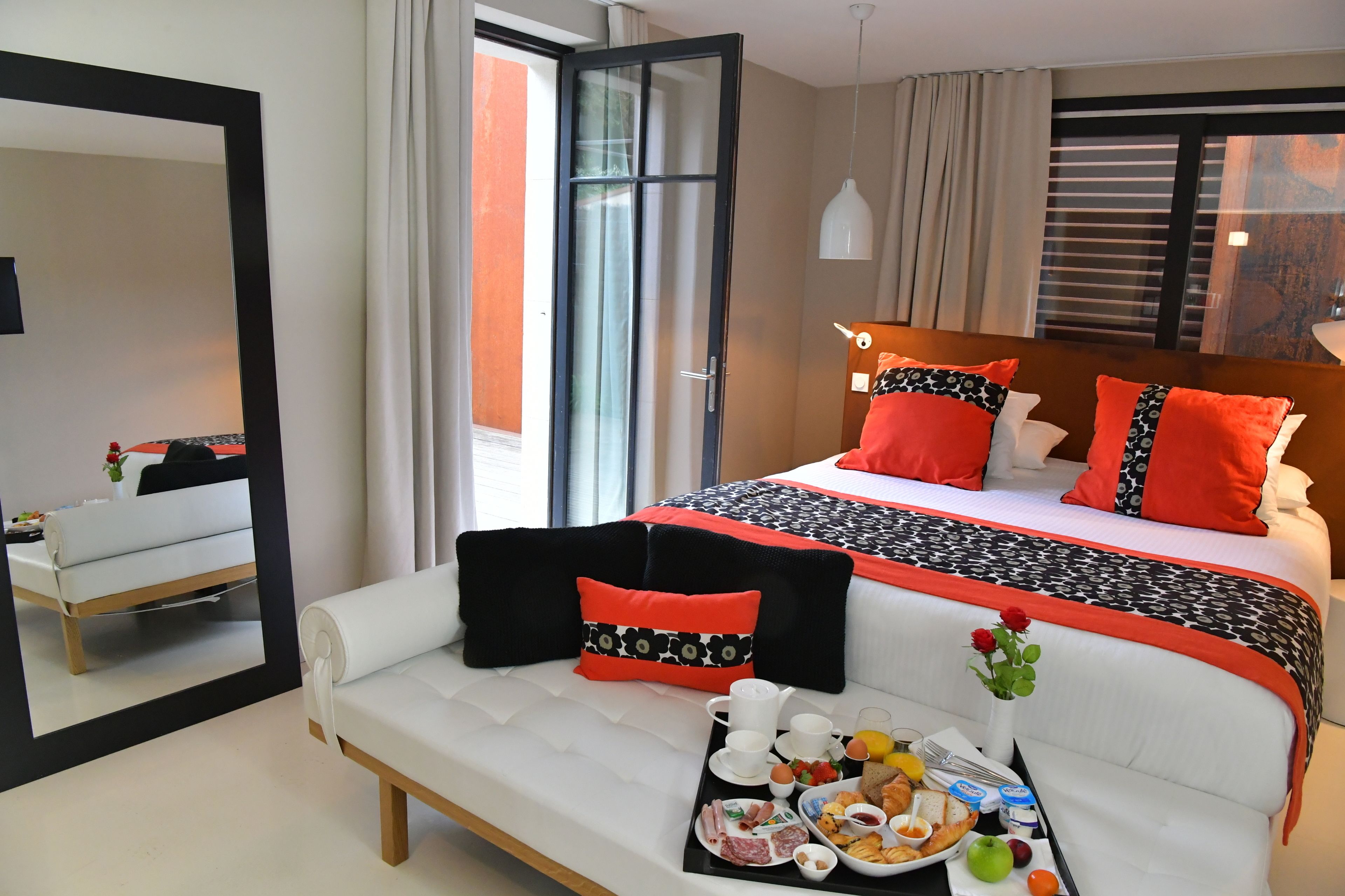 A modern hotel room with a large bed, white sofa, breakfast tray, and a mirror reflecting the room.