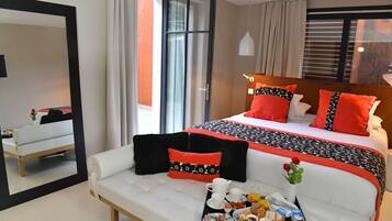 A modern hotel room with a large bed, white sofa, breakfast tray, and a mirror reflecting the room.