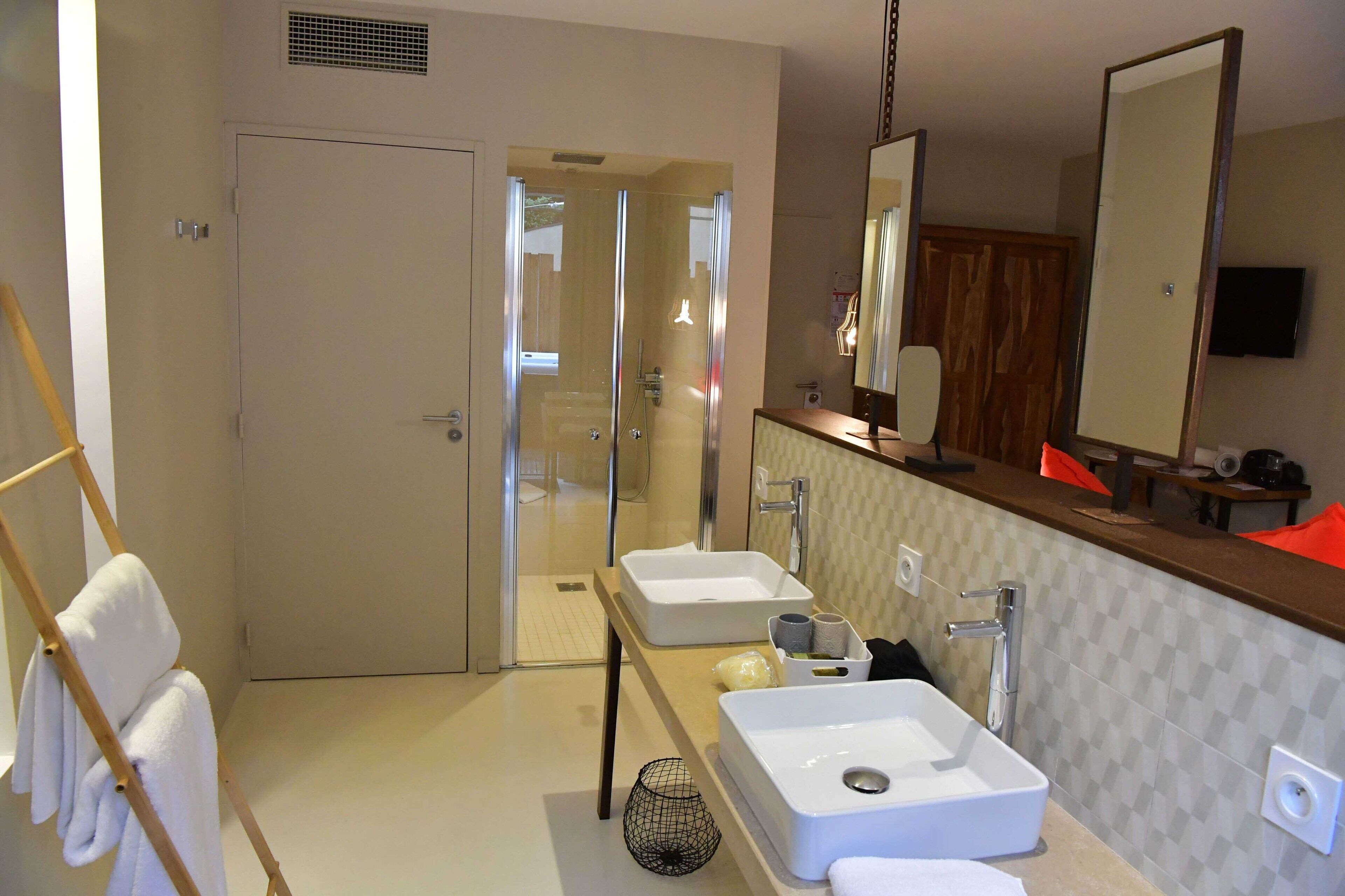 A modern bathroom with two sinks, a shower, and a large mirror.