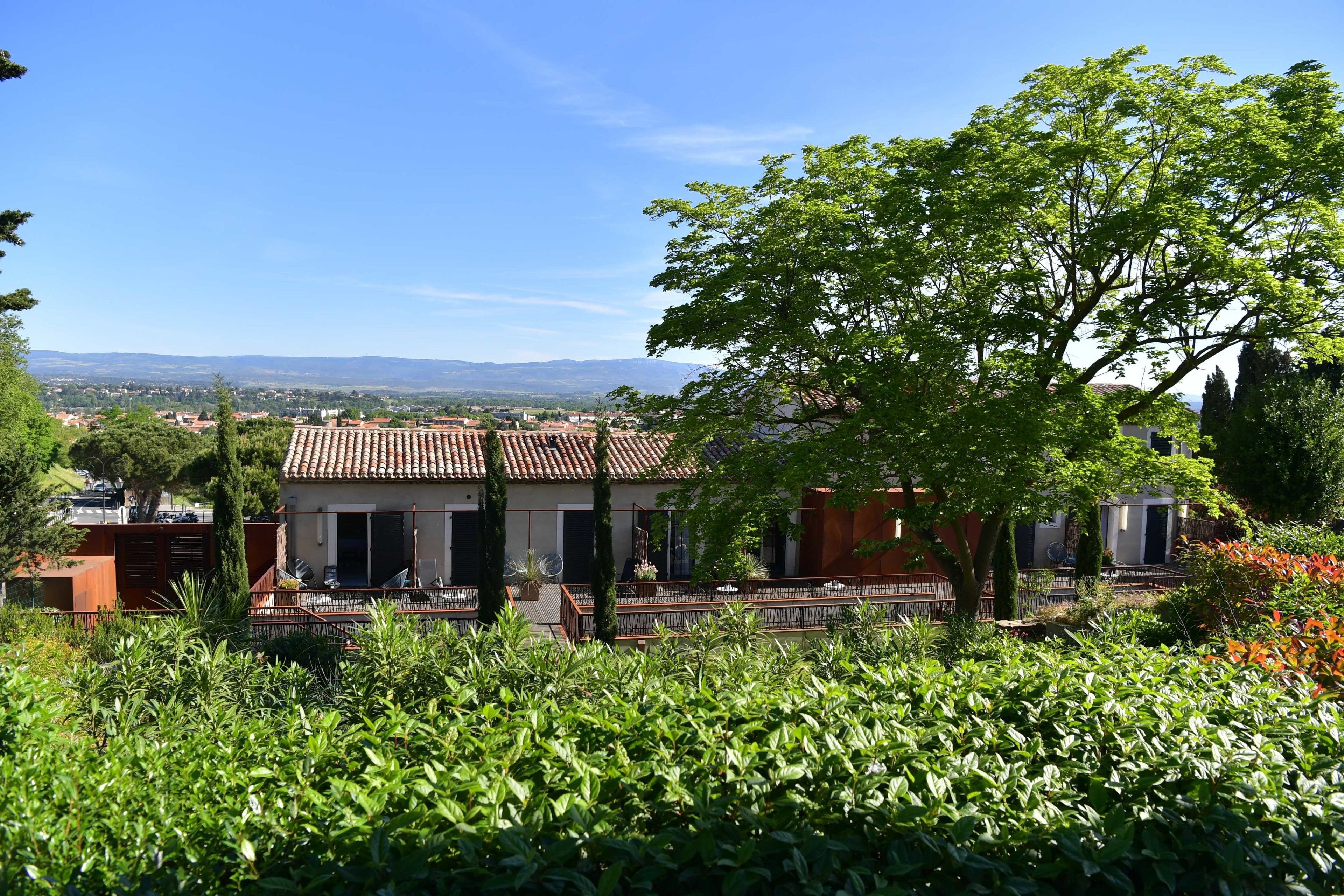 A villa with a tiled roof, surrounded by lush greenery and a view of distant hills.