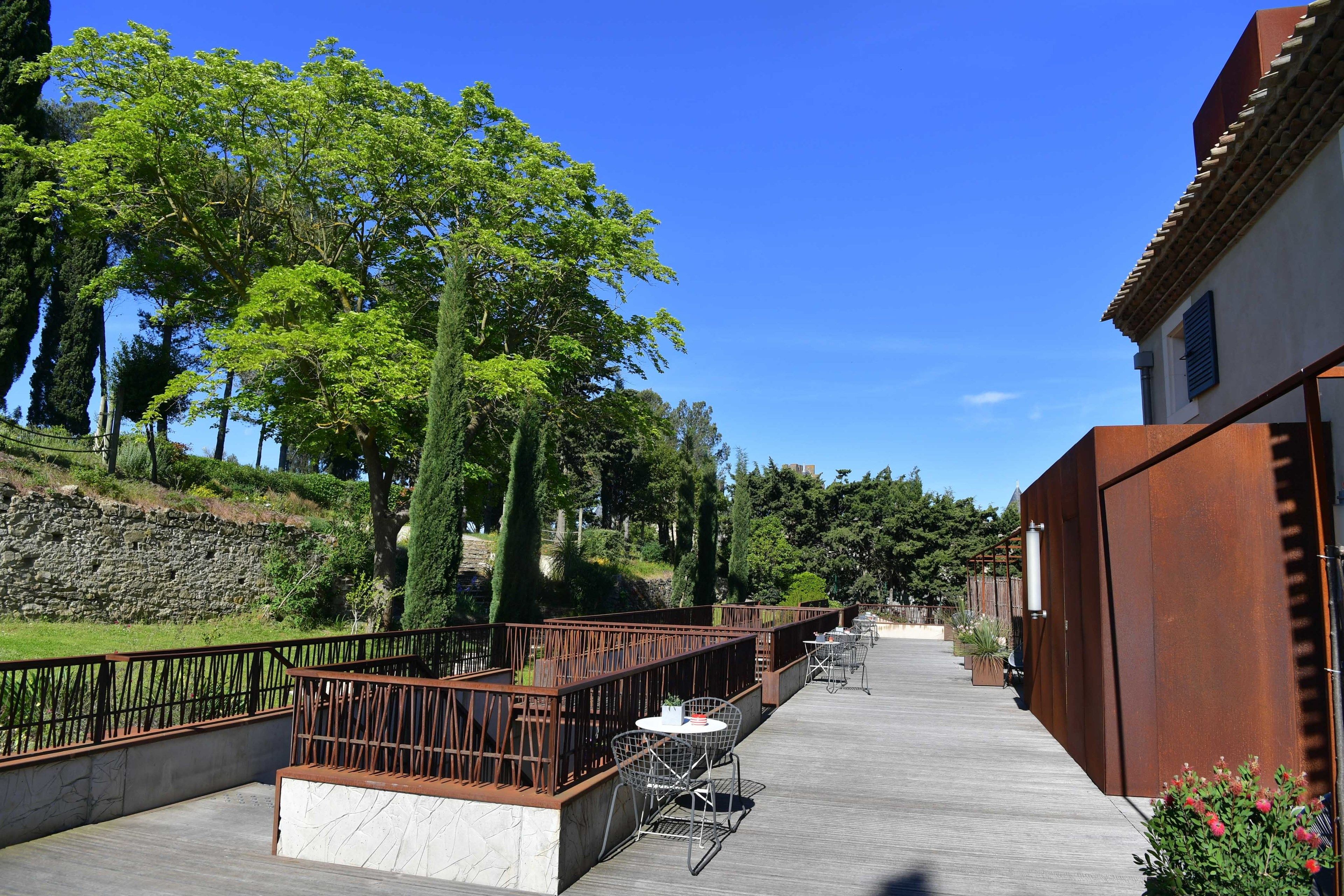 A wooden deck with outdoor seating, surrounded by greenery and a stone wall.