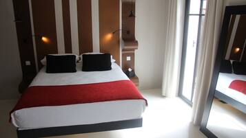 Habitación de hotel con una cama grande, un cabecero de madera, una ventana con cortinas y un espejo en la pared.