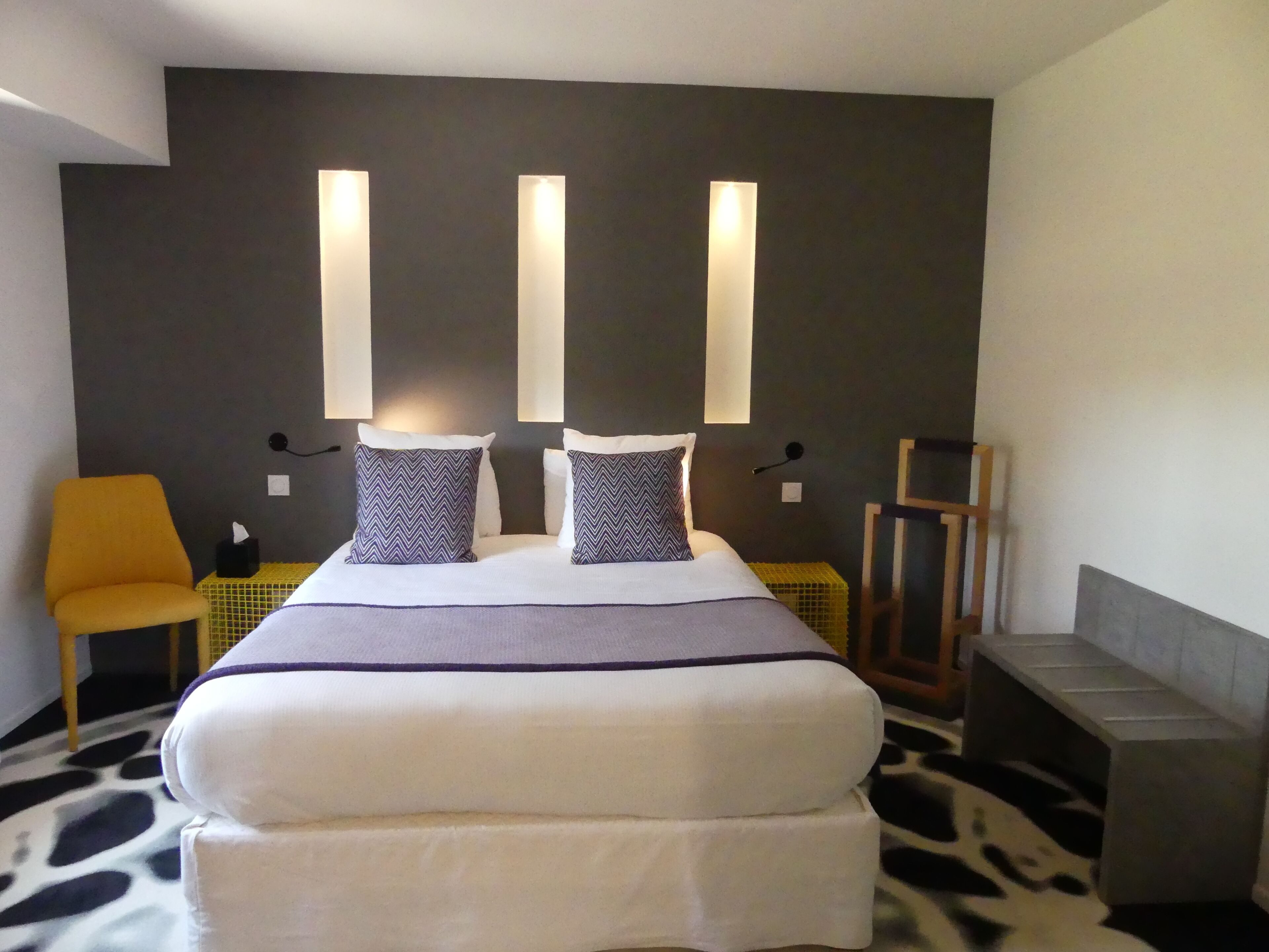A modern hotel room with a large bed, two bedside lamps, a chair, and a small table.