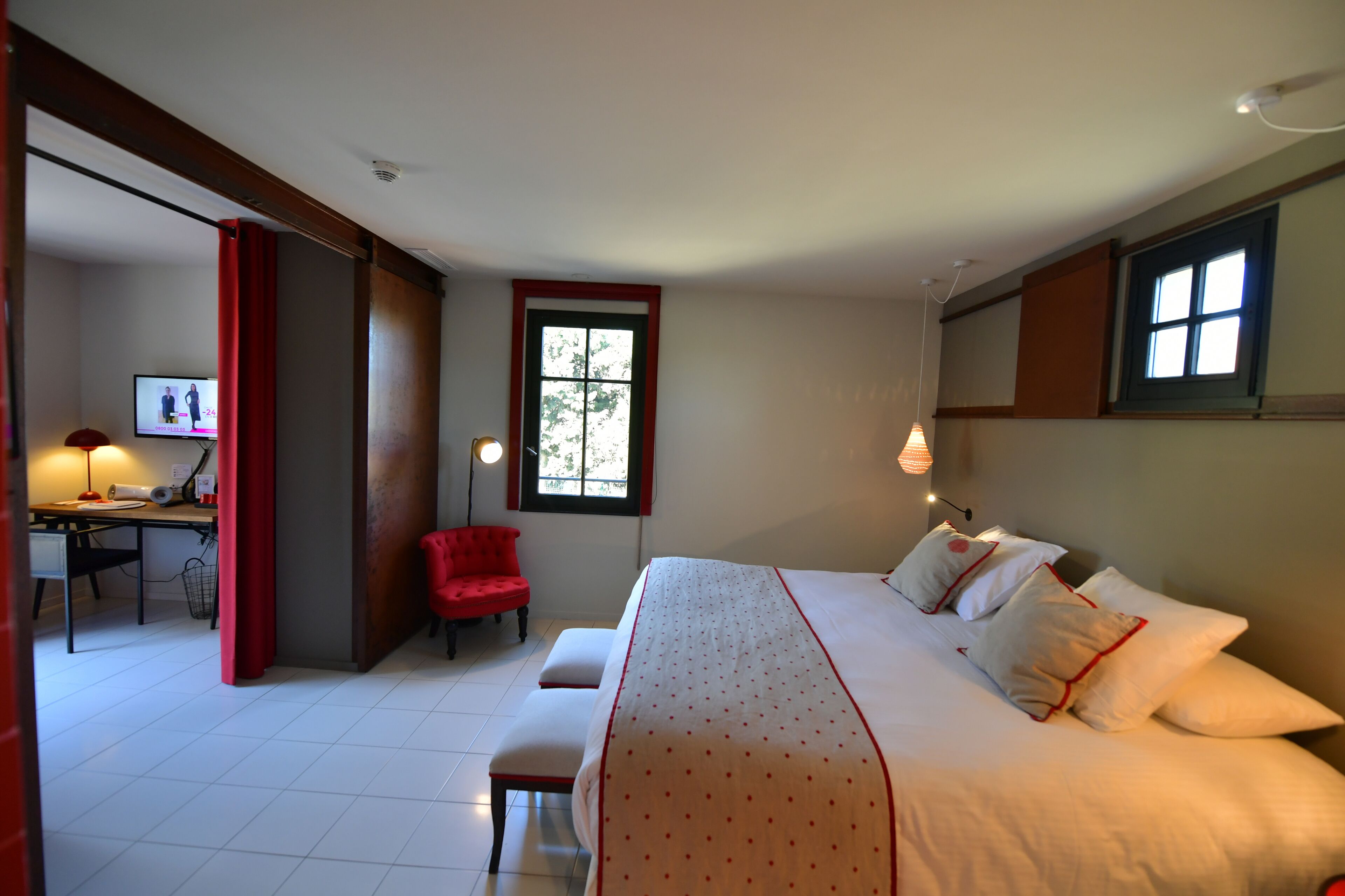 A bedroom with a large bed, a desk with a chair, a red chair, and a television.
