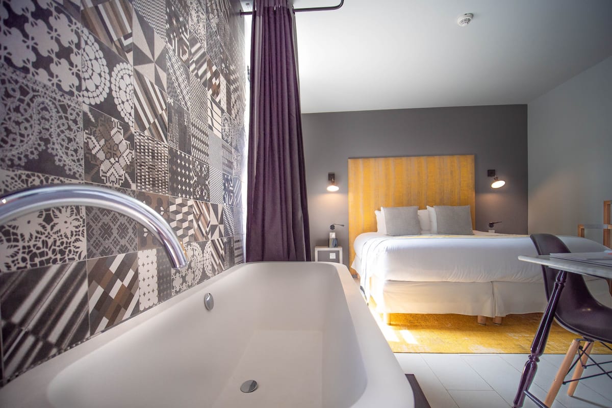 Una habitación de hotel moderna con una bañera grande, una cama bien hecha y una pequeña mesa con una silla.