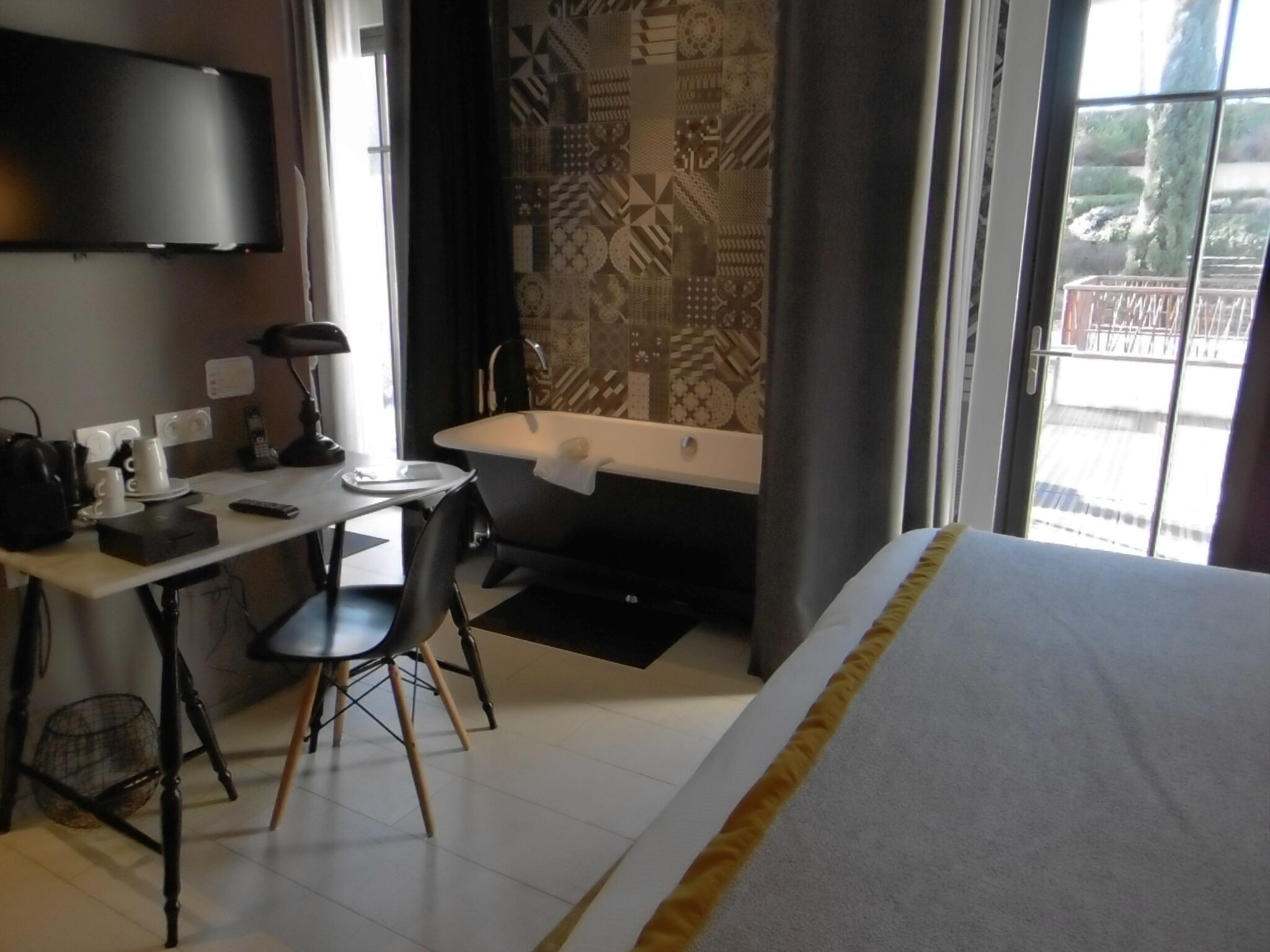 A hotel room with a bed, a desk with a chair, a sink, and a television mounted on the wall.