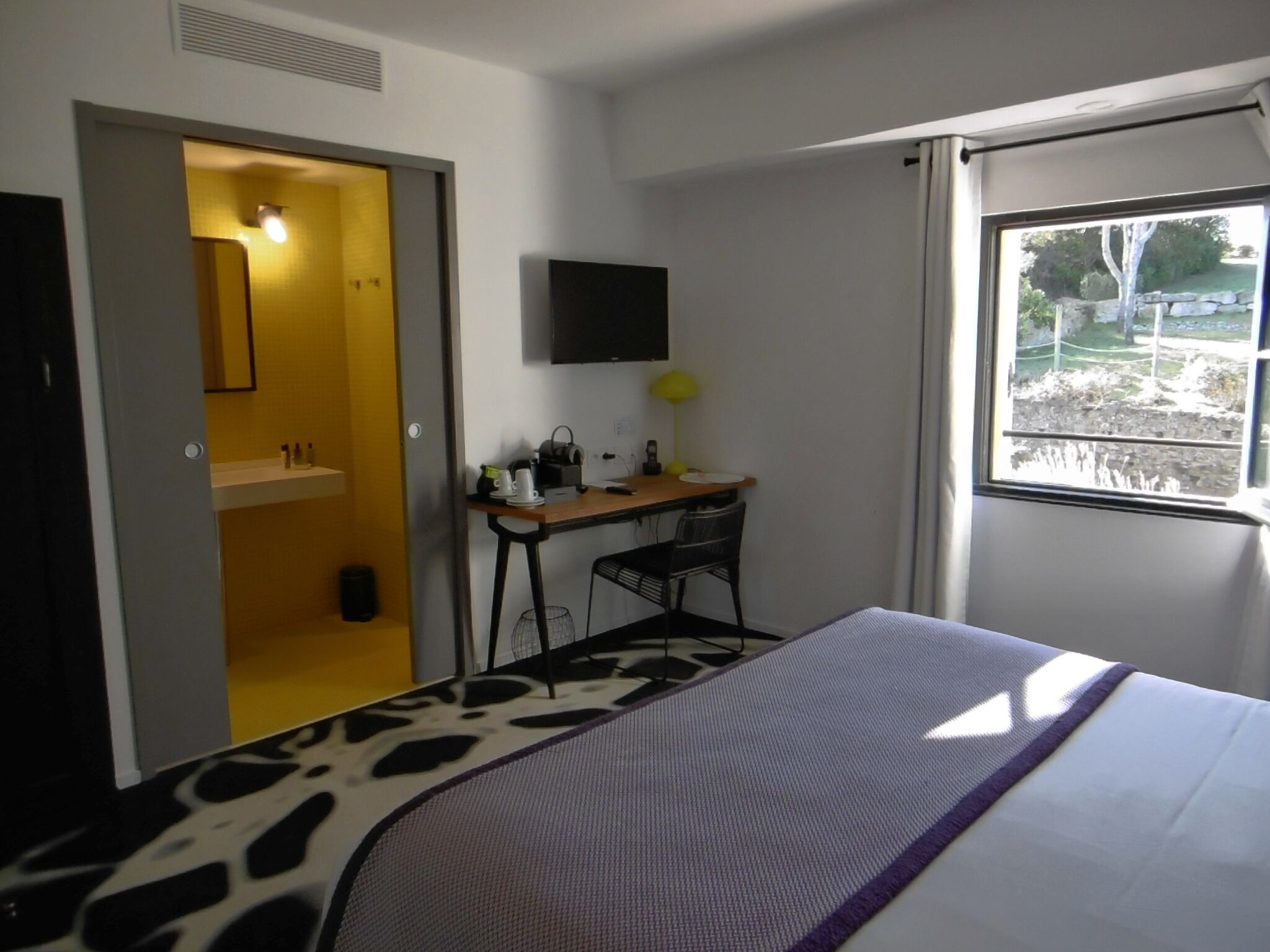 Habitación de hotel con cama, escritorio, silla, televisor y ventana con vista al exterior.