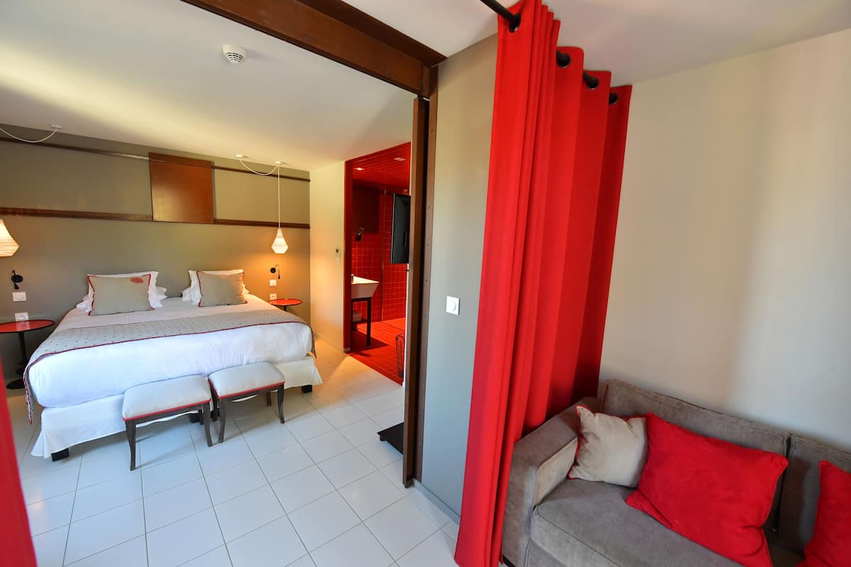 Habitación de hotel con cama, mesitas de noche, un banco, un sofá y una cortina roja.
