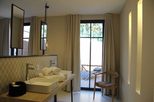 A bathroom with a large mirror, two sinks, a towel rack, and a chair near a sliding glass door leading to a balcony.